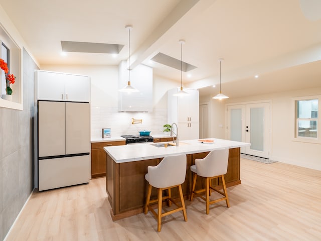 kitchen with white cabinetry, a center island with sink, hanging light fixtures, and light wood-type flooring