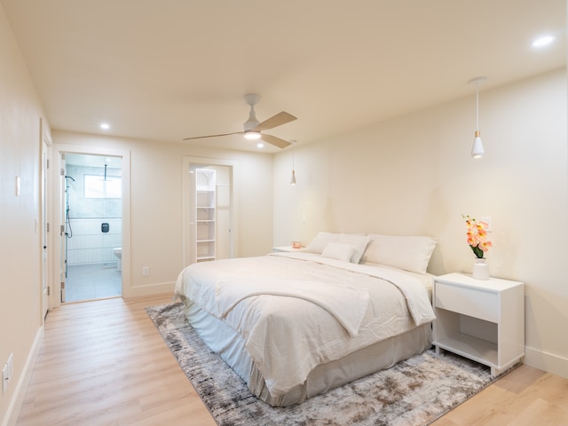 bedroom featuring ensuite bath, a walk in closet, light wood-type flooring, and ceiling fan