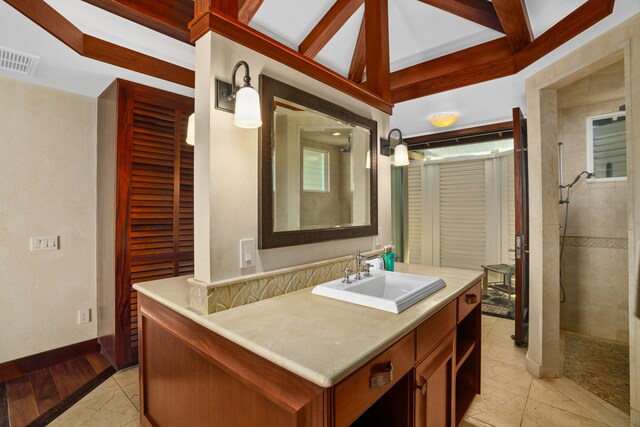 bathroom with tiled shower, beam ceiling, tile patterned flooring, and vanity