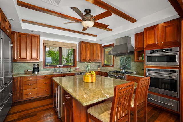 kitchen with wall chimney range hood, backsplash, dark hardwood / wood-style flooring, light stone counters, and a center island