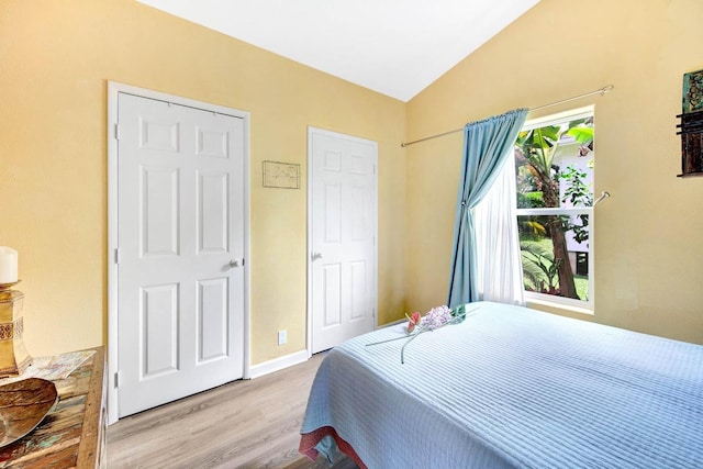 bedroom with vaulted ceiling, wood finished floors, and baseboards