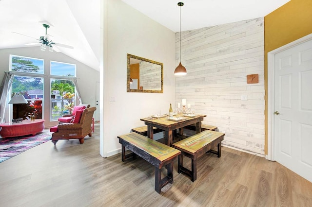 dining room featuring a ceiling fan, high vaulted ceiling, wooden walls, and light wood finished floors