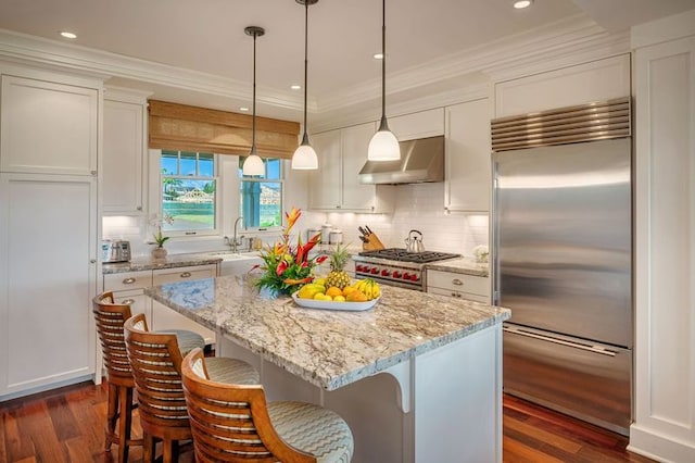 kitchen with a center island, wall chimney exhaust hood, dark hardwood / wood-style floors, white cabinetry, and premium appliances