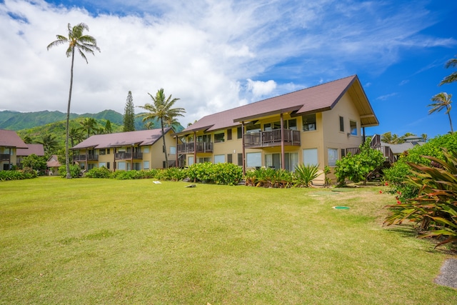 back of property with a balcony, a mountain view, and a yard