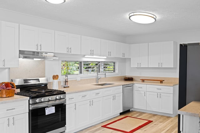 kitchen with appliances with stainless steel finishes, white cabinetry, sink, light wood-type flooring, and a textured ceiling