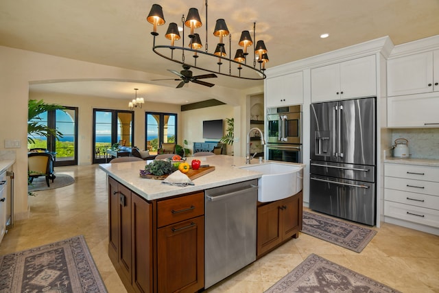 kitchen with ceiling fan with notable chandelier, sink, an island with sink, appliances with stainless steel finishes, and white cabinets