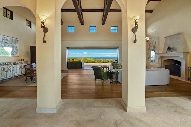 interior space featuring plenty of natural light, a towering ceiling, light wood-type flooring, and beam ceiling