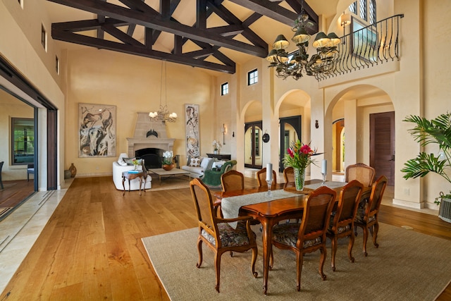 dining space featuring light wood-type flooring, a fireplace with raised hearth, high vaulted ceiling, and a notable chandelier