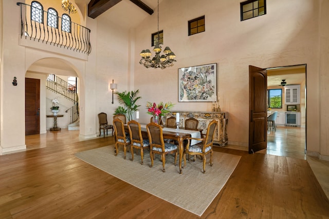 dining space with wine cooler, beamed ceiling, ceiling fan with notable chandelier, light hardwood / wood-style floors, and high vaulted ceiling