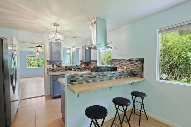 kitchen featuring decorative light fixtures, stainless steel fridge, kitchen peninsula, island range hood, and a breakfast bar