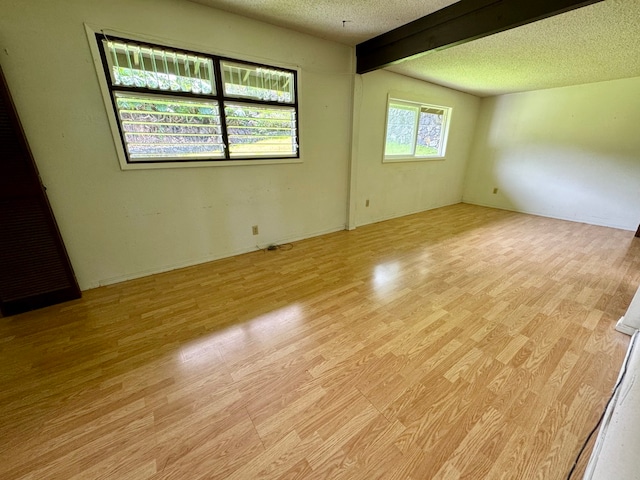 unfurnished room with a textured ceiling, light wood-type flooring, and beam ceiling