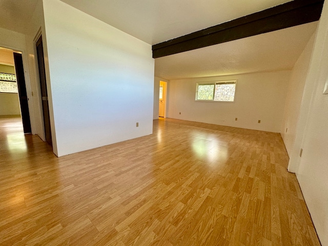 unfurnished room with beam ceiling and light hardwood / wood-style floors