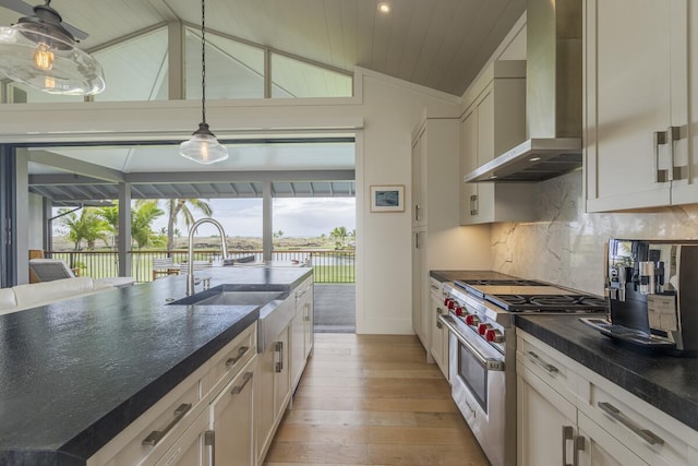 kitchen with a sink, stainless steel range, vaulted ceiling, dark countertops, and wall chimney exhaust hood