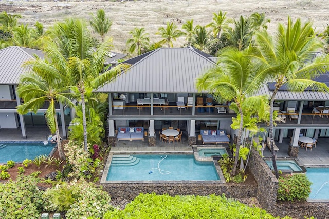 back of house with a balcony, a pool with connected hot tub, and a patio