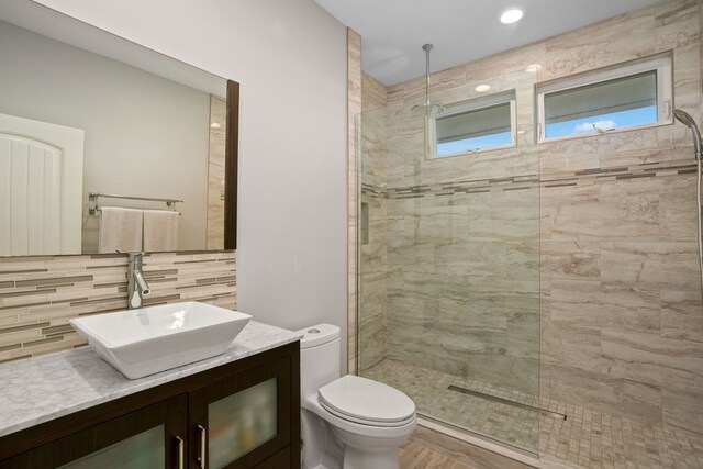 bathroom with vanity, backsplash, tiled shower, tile walls, and toilet