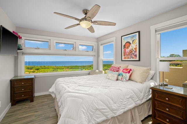 bedroom featuring light wood-type flooring, multiple windows, ceiling fan, and a water view