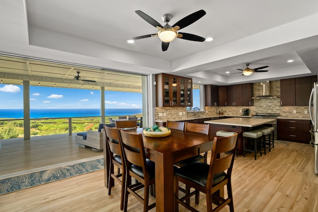 dining area with a raised ceiling, light hardwood / wood-style flooring, ceiling fan, and a water view