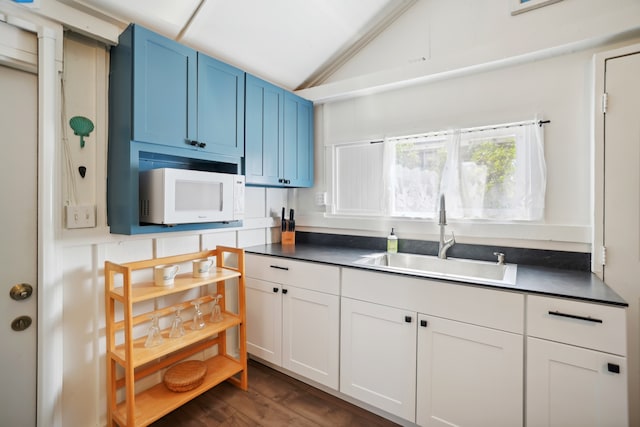 kitchen featuring blue cabinetry, vaulted ceiling, white cabinetry, sink, and dark wood-type flooring