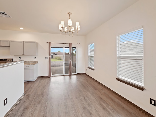 unfurnished dining area featuring a healthy amount of sunlight, an inviting chandelier, and light hardwood / wood-style flooring