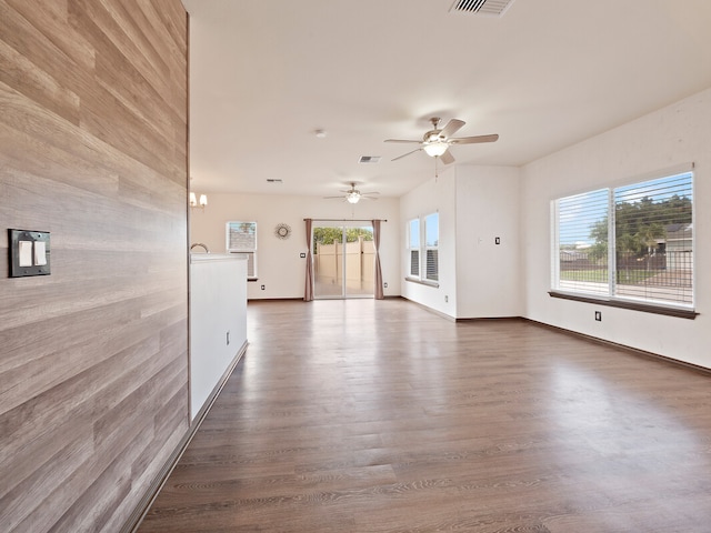 unfurnished living room featuring ceiling fan with notable chandelier, dark hardwood / wood-style floors, and a healthy amount of sunlight