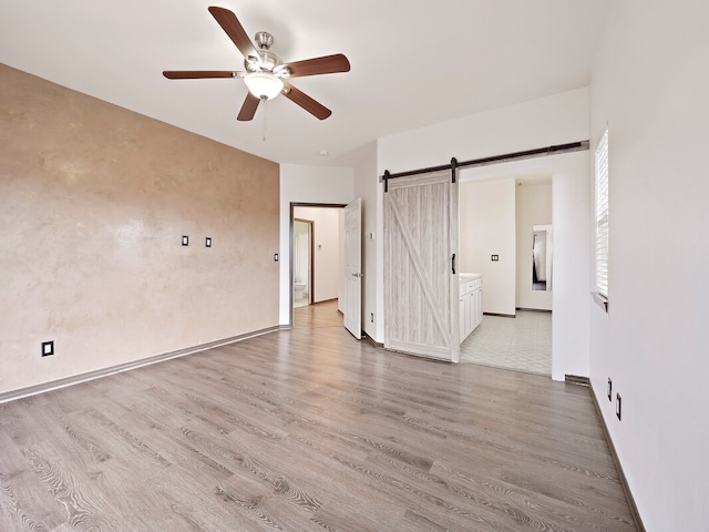 interior space with light wood-type flooring, ceiling fan, and a barn door