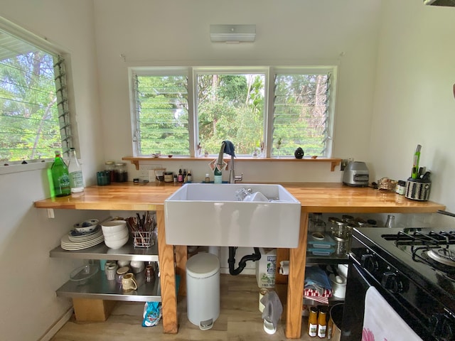 kitchen featuring wood-type flooring, gas stove, sink, and wooden counters