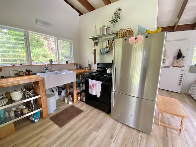 kitchen featuring light wood-type flooring, stainless steel refrigerator, sink, and black gas range