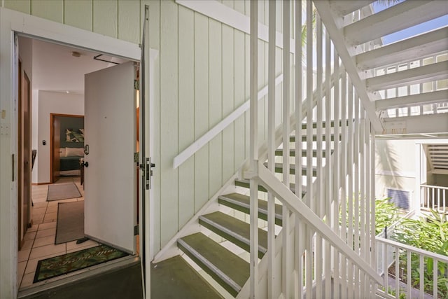 stairway with wood walls and tile patterned floors