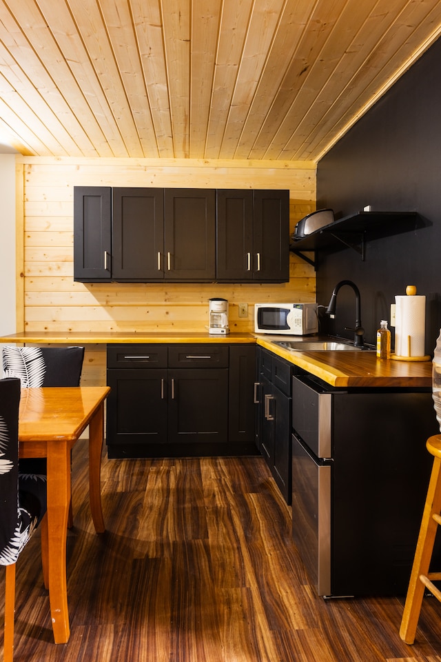 kitchen featuring dark hardwood / wood-style flooring, wood ceiling, sink, stainless steel refrigerator, and wood walls