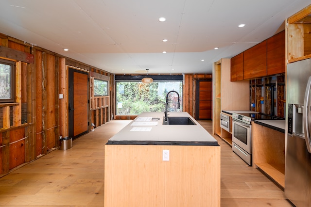 kitchen with a kitchen island with sink, sink, hanging light fixtures, appliances with stainless steel finishes, and light hardwood / wood-style floors