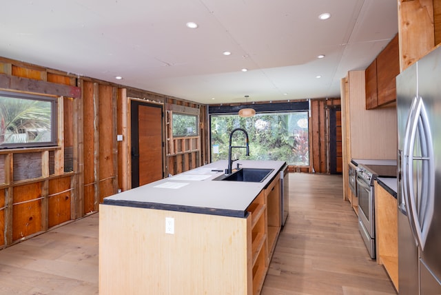 kitchen featuring light hardwood / wood-style flooring, stainless steel appliances, sink, wood walls, and a kitchen island with sink