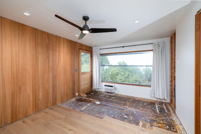 empty room with light hardwood / wood-style flooring, ceiling fan, wood walls, and a wall mounted air conditioner