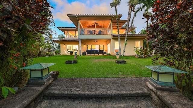 back house at dusk with a yard, ceiling fan, an outdoor living space with a fire pit, and a patio