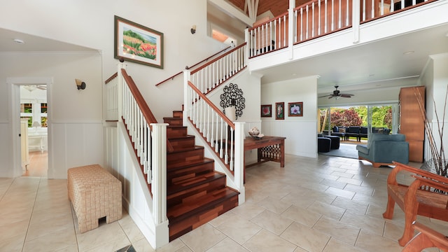 staircase featuring a towering ceiling, ceiling fan, and ornamental molding