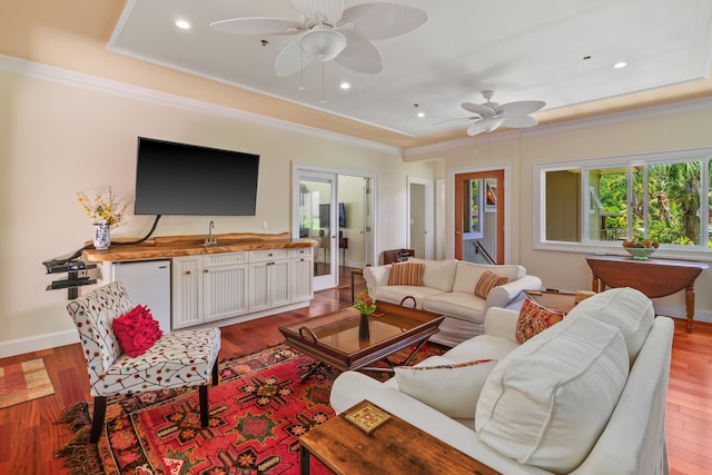 living room with light wood-type flooring, ornamental molding, ceiling fan, a tray ceiling, and french doors