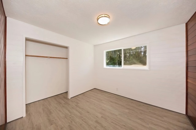 unfurnished bedroom with light hardwood / wood-style floors, a textured ceiling, wood walls, and a closet