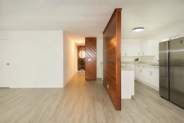 kitchen with light wood-type flooring, stainless steel fridge, white cabinets, and wooden walls