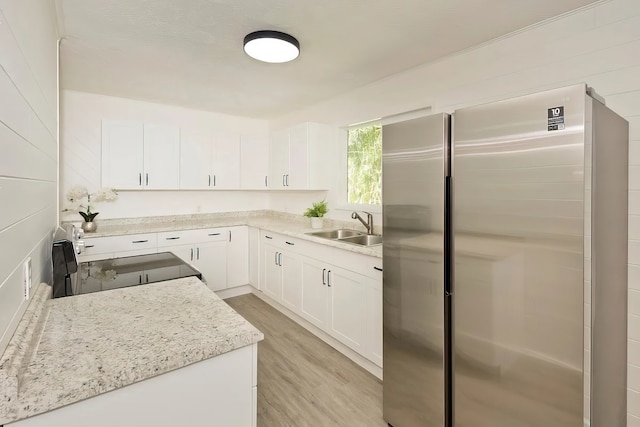 kitchen with white cabinets, light stone counters, stainless steel appliances, light hardwood / wood-style floors, and sink