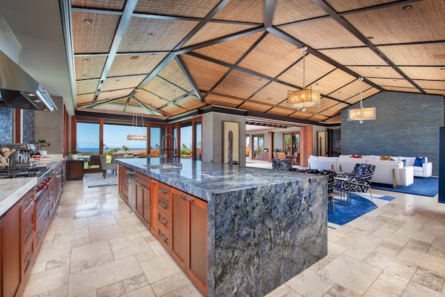 kitchen featuring a spacious island, range hood, hanging light fixtures, sink, and dark stone counters