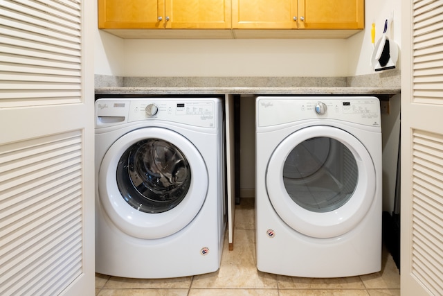 washroom featuring independent washer and dryer, light tile patterned floors, and cabinets