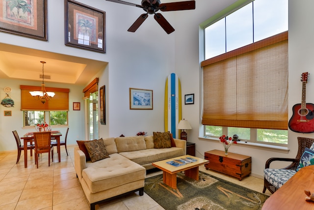 tiled living room with a raised ceiling, ceiling fan with notable chandelier, and a healthy amount of sunlight