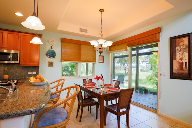 dining area with a notable chandelier, a tray ceiling, and light tile patterned floors