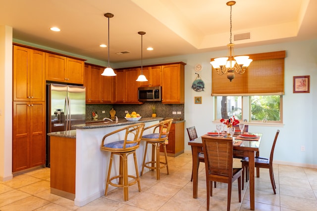 kitchen with pendant lighting, a raised ceiling, backsplash, appliances with stainless steel finishes, and a center island