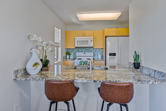 kitchen with white appliances, light brown cabinetry, kitchen peninsula, and a breakfast bar