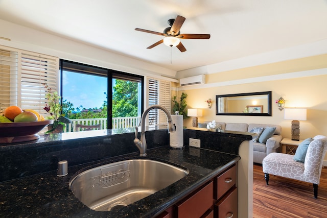 kitchen with dark stone counters, a wall unit AC, sink, ceiling fan, and dark hardwood / wood-style floors