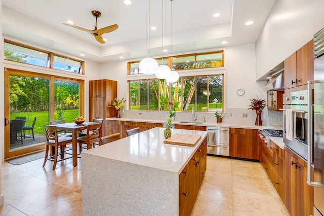 kitchen with pendant lighting, a tray ceiling, a kitchen island, sink, and stainless steel appliances