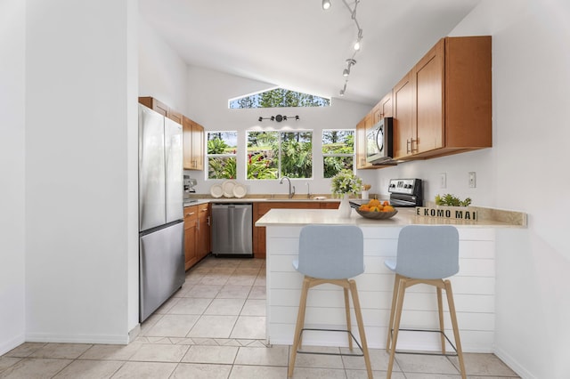 kitchen featuring appliances with stainless steel finishes, light tile patterned flooring, a kitchen breakfast bar, and vaulted ceiling