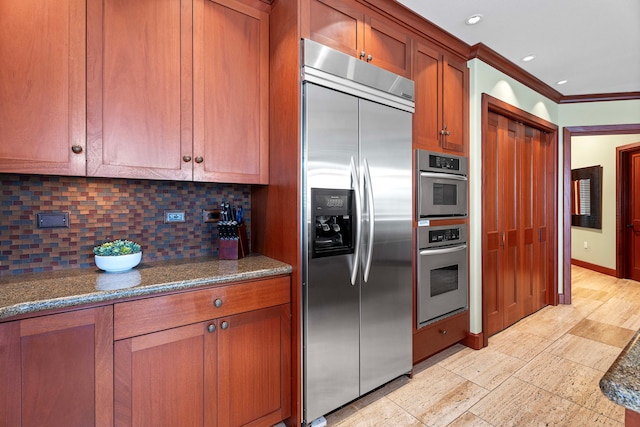 kitchen with dark stone counters, brown cabinets, decorative backsplash, stainless steel appliances, and ornamental molding