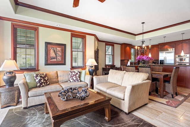 living area with a raised ceiling, ceiling fan with notable chandelier, and crown molding