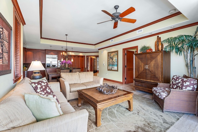living room with crown molding, visible vents, a tray ceiling, baseboards, and ceiling fan with notable chandelier